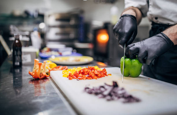 Chef in black latex gloves cutting vegetables in his kitchen in restaurant.